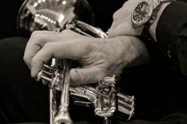 Trompettiste en noir et blanc, gros plan sur la main posée sur les pistons d’un cornet