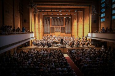 Public assis dans une salle de concert, face à un orchestre sur scène