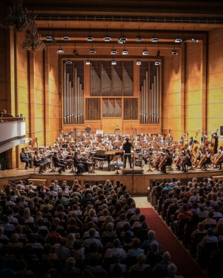 Public assis dans une salle de concert, face à un orchestre sur scène