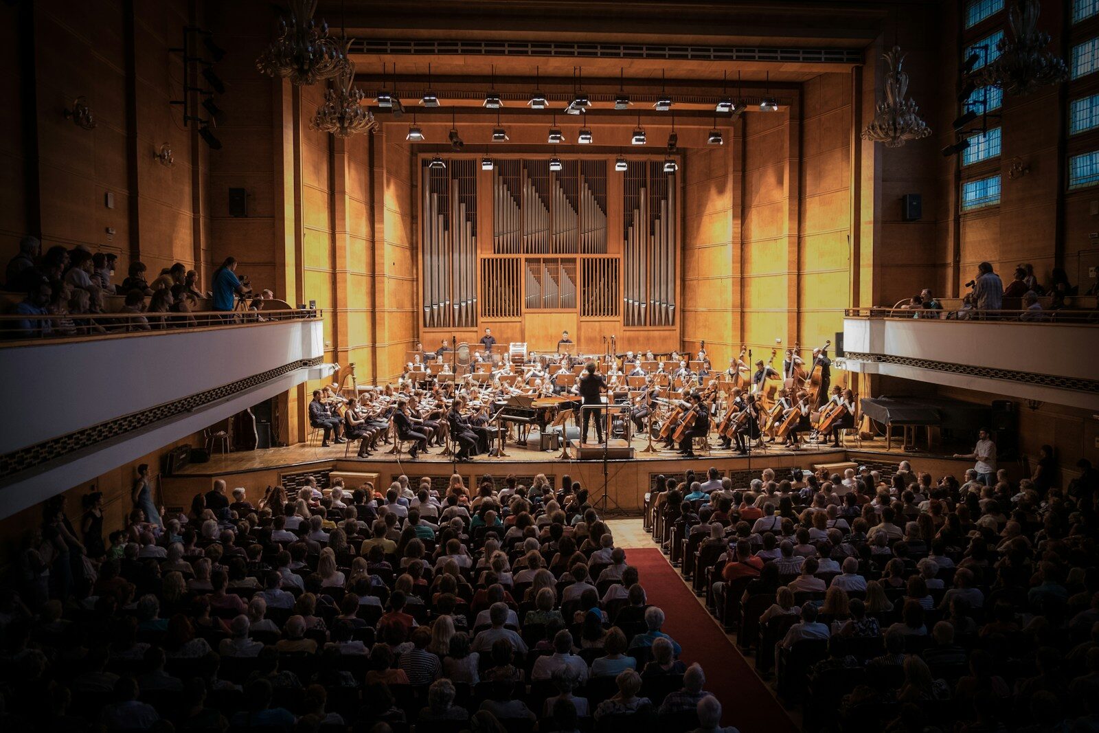 Public assis dans une salle de concert, face à un orchestre sur scène